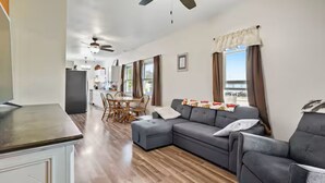 En moderne stue med en grå hjørnesofa, et spiseområde med bord og stole, samt et køkken med et køleskab.
