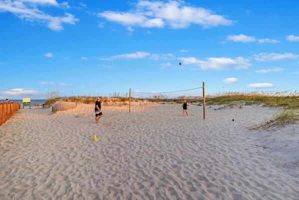 Ein Sandstrand mit einem Volleyballnetz, einem Holzzaun und einer Rasenfläche.