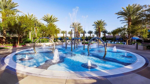 A circular pool with multiple fountains and palm trees around it.