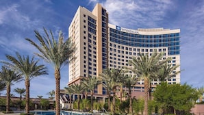 A modern hotel with a curved facade, multiple floors, and a pool area with palm trees.