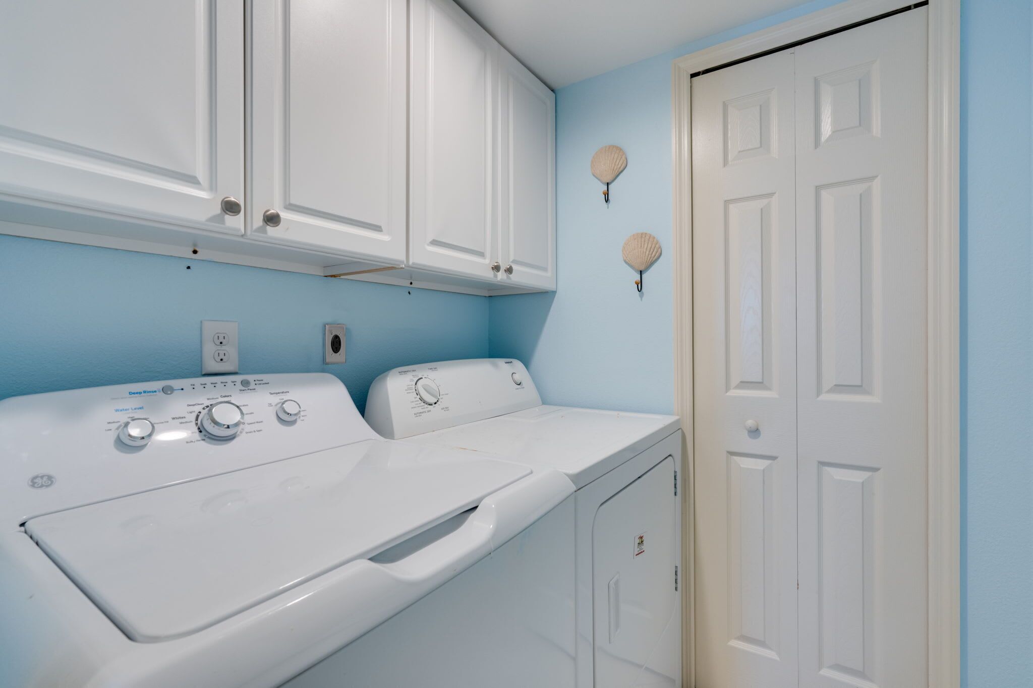 A laundry room with a front-loading washer and dryer, white cabinets, and a door with a handle.