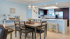 A modern kitchen with dark cabinets, a central island, and a dining area with a wooden table and chairs. - Gorgeous Punta Rassa Condo 504 - River and Sunset views! (Fort Myers)