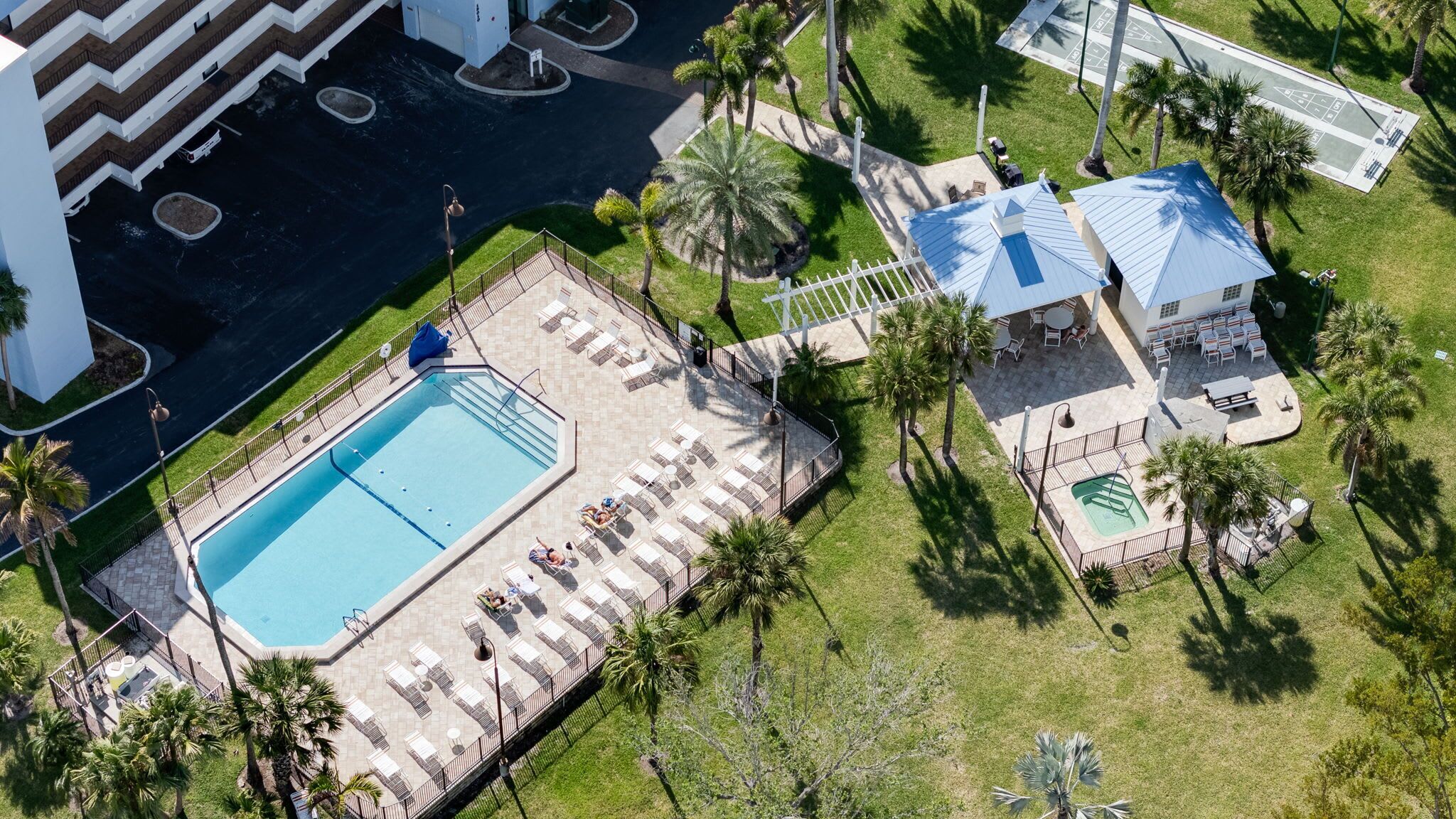 Vista aérea de un hotel con piscina, tumbonas y una pequeña zona de estar al aire libre rodeada de palmeras.
