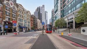 Eine Stadtstraße mit Busspur, ein Bus der anfährt, und Gebäuden, darunter ein moderner Glaswolkenkratzer.