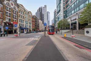 Eine Stadtstraße mit Busspur, ein Bus der anfährt, und Gebäuden, darunter ein moderner Glaswolkenkratzer.