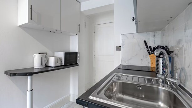Eine moderne Küche mit schwarzem Arbeitsplatz, einer Edelstahlspüle, einer Mikrowelle und einem Wasserkocher.
