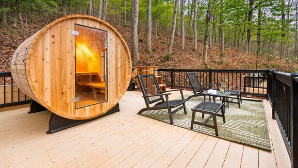 Une cabane en bois avec une porte en verre, un espace salon extérieur et une terrasse donnant sur une forêt.