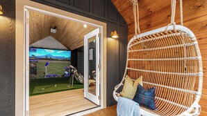 Une terrasse en bois avec un fauteuil suspendu et un téléviseur diffusant un match de golf.
