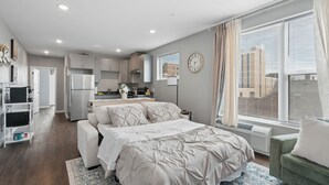A modern apartment with a bedroom, kitchenette, and a large window with a city view. - Valclyde Cozy Suite-Sleeps 4-Downtown-MPLs (Minneapolis)