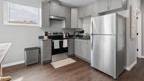 A modern kitchen with grey cabinets, stainless steel appliances, a window, and a small trash bin. - Valclyde Cozy Suite-Sleeps 4-Downtown-MPLs (Minneapolis)