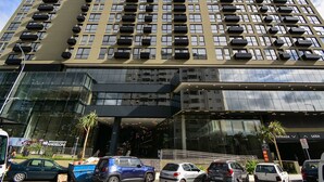 Un bâtiment moderne à plusieurs étages, doté de grandes fenêtres et d’un parking où sont stationnées plusieurs voitures.