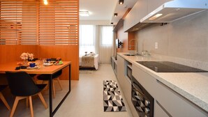 A modern kitchen with a dining area, a built-in stove, and a window with curtains. - Studio em frente a UFSC e HU - 106A VIVA (Florianópolis)