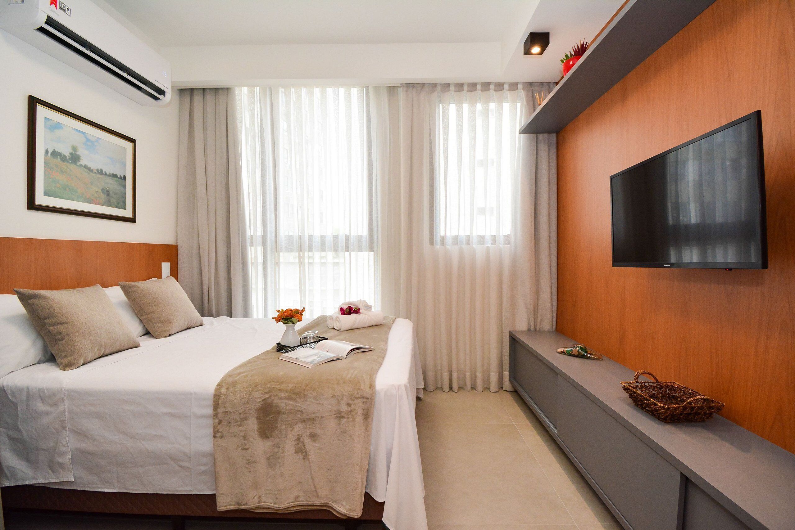 A hotel room with a bed, a flat-screen TV, a bedside table, and a large window with curtains.