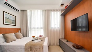 Une chambre d’hôtel équipée d’un lit, d’un téléviseur à écran plat, d’une table de chevet et d’une grande fenêtre avec des rideaux.