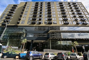 Un edificio de varios pisos con fachada moderna, grandes ventanales y un estacionamiento con varios vehículos.