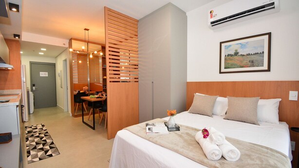 A hotel room with a bed, a desk, a chair, a dining area, and an air conditioning unit. - Studio em frente a UFSC e HU - 106A VIVA (Florianópolis)