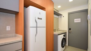 A compact kitchen with a refrigerator, washing machine, and a small countertop. - Studio em frente a UFSC e HU - 106A VIVA (Florianópolis)