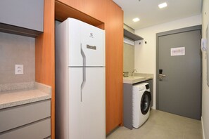 A compact kitchen with a refrigerator, washing machine, and a small countertop. - Studio em frente a UFSC e HU - 106A VIVA (Florianópolis)