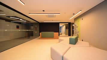 A modern lobby with glass walls, a reception desk, and a seating area with cushions.