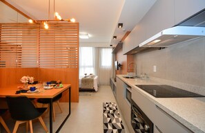 Een moderne keuken met een ingebouwde kookplaat, een eethoek met een tafel voor twee personen en een slaapkamer met een bed en raam.