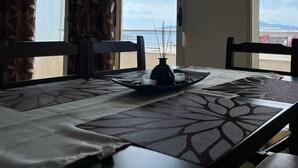 Un comedor con una mesa lista para dos, un florero con velas y vista al mar a través de amplias ventanas.