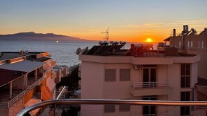 Un edificio costero con terraza en la azotea y vistas al mar, con un atardecer.