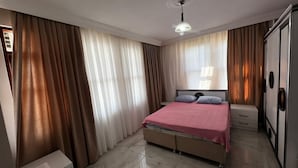 A bedroom with a bed, curtains, a wardrobe, and a ceiling light.