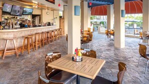 A bar area with multiple stools and a counter, a table with a bottle of condiments, and outdoor seating with umbrellas. - Island Comfort: 2BR at Wyndham Kona Coast Resort (Kailua-Kona)