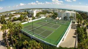 Tenniskenttä, jonka ympärillä on palmuja ja rakennuksia.