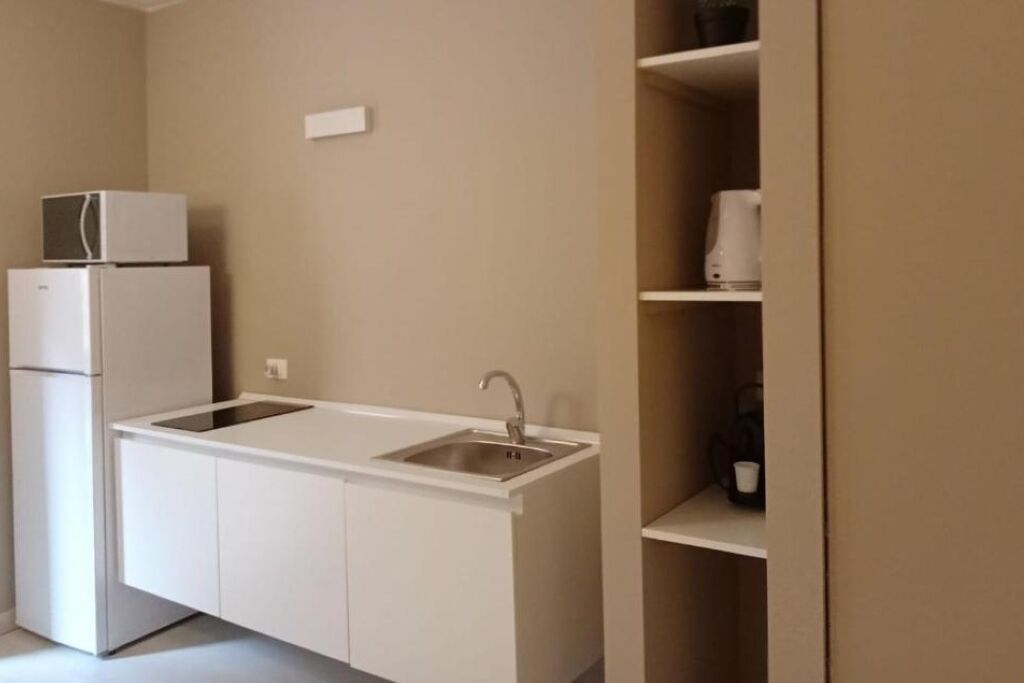 Una cocina compacta con armarios blancos, un lavamanos integrado y un microondas encima de un refrigerador.