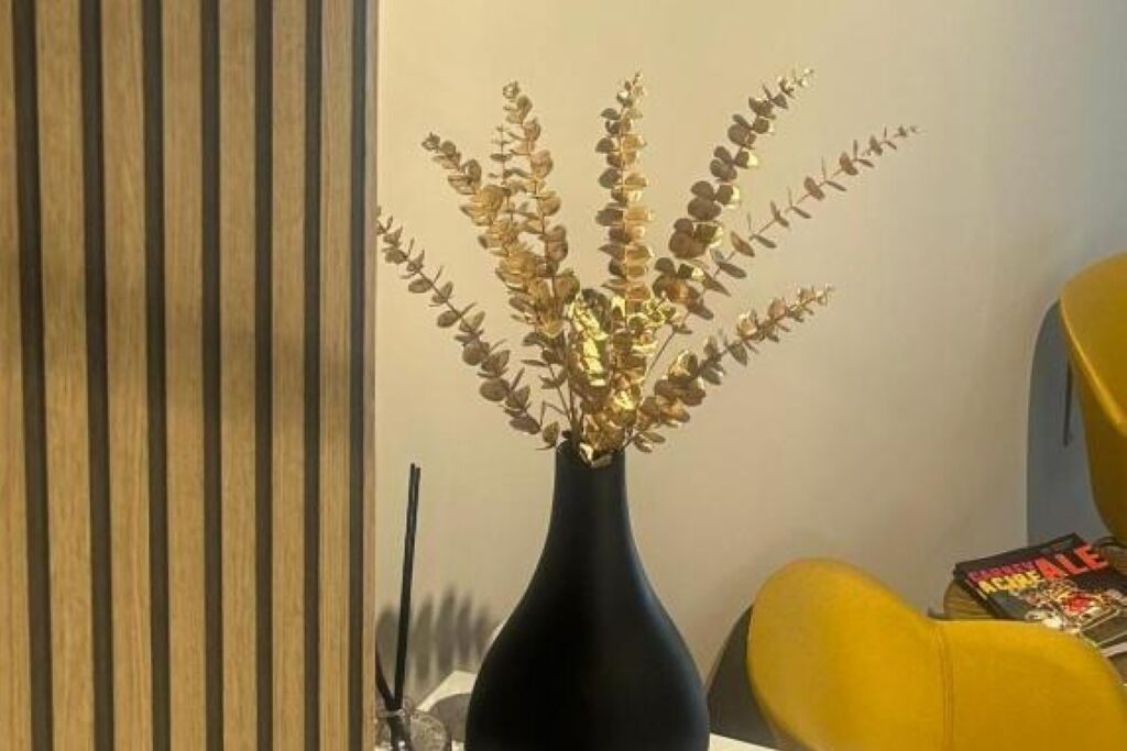 A room with a dark vase containing a plant, a striped wall, and a yellow chair.