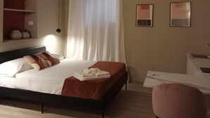 Ein Hotelzimmer mit Bett, Sessel, Schreibtisch und einem fenster mit Vorhängen.