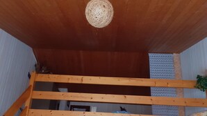 Un interno in legno con un lampadario sferico sospeso, una zona notte soppalcata e una cucina con frigorifero e mobili.