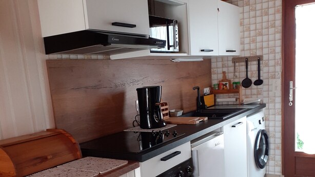 Cucina compatta con mobili bianchi, microonde, macchina da caffè, piano cottura e lavatrice.