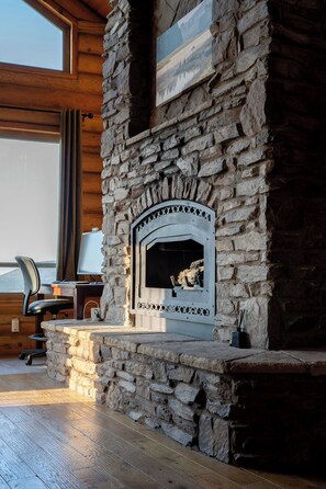 A stone fireplace with a chimney, a wooden desk with a chair, and a view of the outdoors.