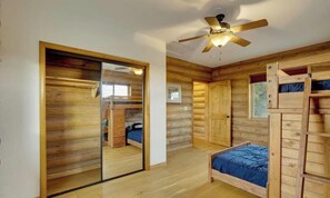 Ein Blockhausszimmer mit Spiegelkleiderschrank, einem Bett, Deckenventilator und einem Fenster.