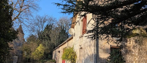 Un edificio rústico de piedra con un sendero de grava que lo lleva hasta él, rodeado de árboles y vegetación.