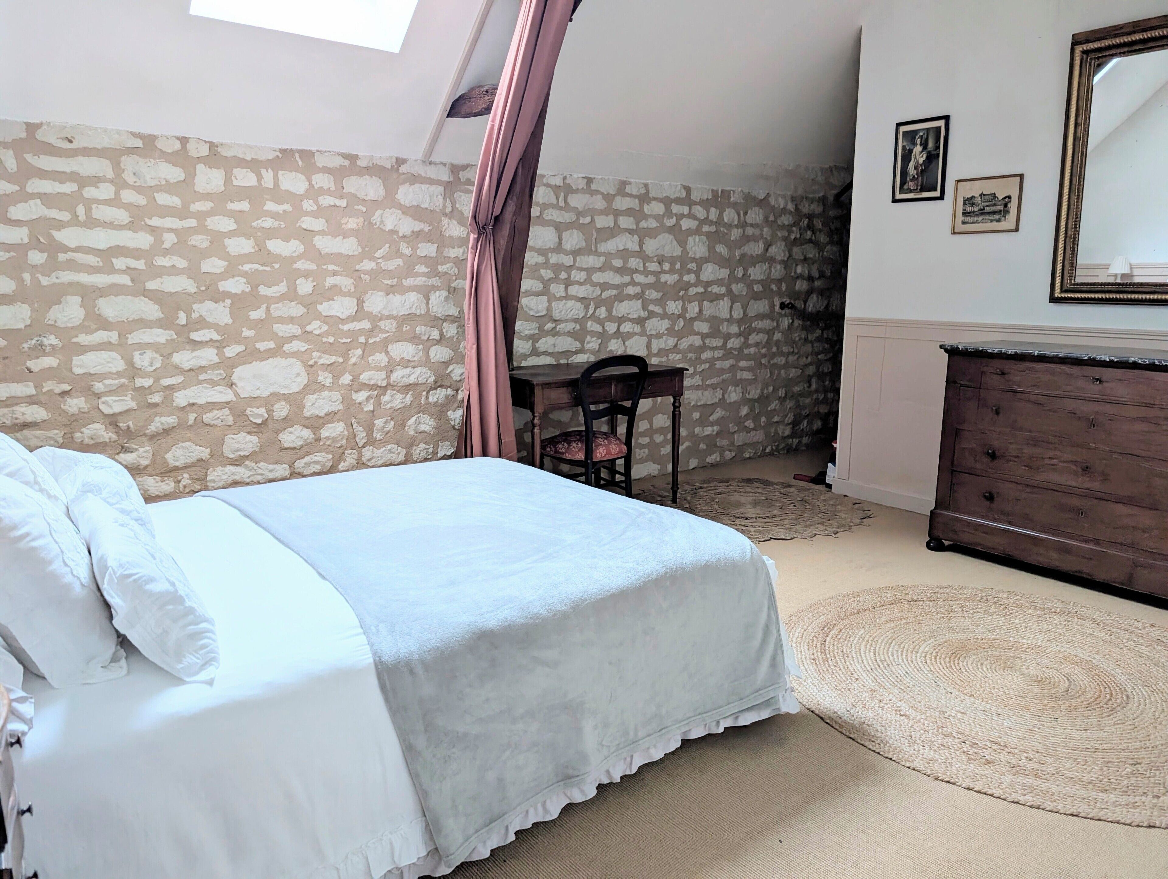 Ein Schlafzimmer mit einer Steinwand, einem Bett mit weißer Bettwäsche, einer Holzkommode und einem Spiegel.