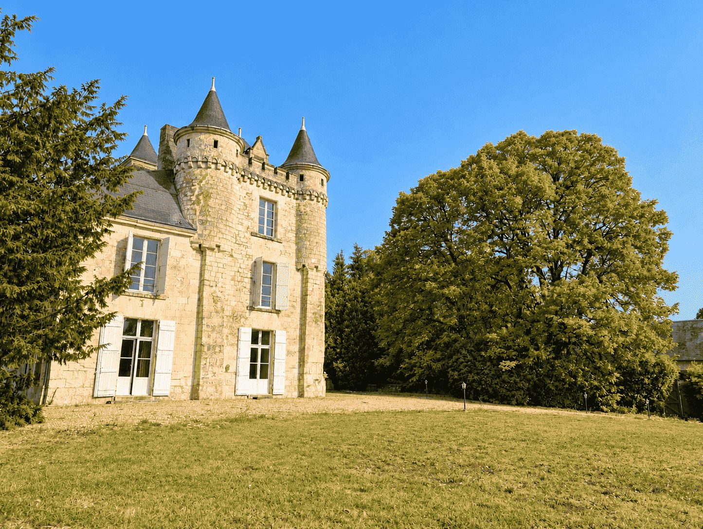 Un bâtiment qui ressemble à un château, avec une tour, entouré d’une zone herbeuse et d’arbres.