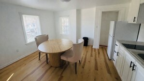 A kitchen with a round wooden table, two chairs, a trash bin, and white cabinets.