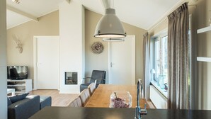 Een moderne keuken met een houten eettafel, een hangende hanglamp en uitzicht op de omgeving door grote ramen.