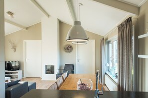 A modern kitchen with a wooden dining table, a hanging pendant light, and a view of the outdoors through large windows. - Luxury bungalow with sauna near beach - 6 persons - Ballum Ameland (Ballum)