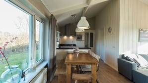 Een moderne keuken met een eethoek, houten vloeren en een groot raam met gordijnen.