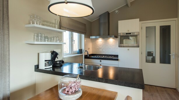 Een moderne keuken met een zwart aanrecht, roestvrijstalen apparatuur en een hangende lamp.