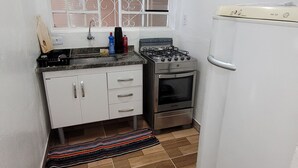 Una cocina compacta con estufa a gas, horno, gabinetes blancos, un ventanal con rejas y piso de baldosas.