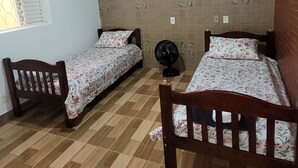 Una habitación con dos camas de madera, un ventilador de pie, una ventana con persianas y una pared de azulejos con recortes circulares.