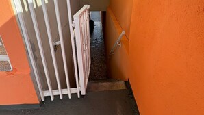 Una escalera estrecha con un portón blanco, un ventanal pequeño y una pared pintada en dos colores.