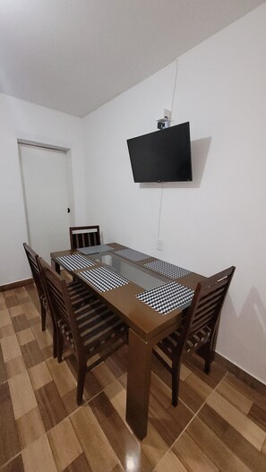 A dining area with a rectangular table, four chairs, a flat-screen TV mounted on the wall, and a door. - House for 5 people / 2 bedrooms / 1 bathroom / garage (Hortolândia)