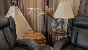 A room with two black leather sofas, a woven basket, a lamp on a wooden side table, and a window with curtains.