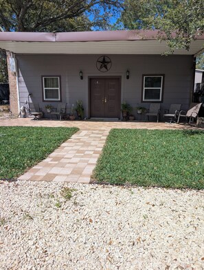 A house with a double door, two windows, a star-shaped decoration above the door, and a paved driveway leading to a lawn.